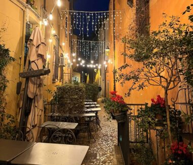 Eine gepflasterte Gasse mit Tischen und Stühlen in der Nacht.